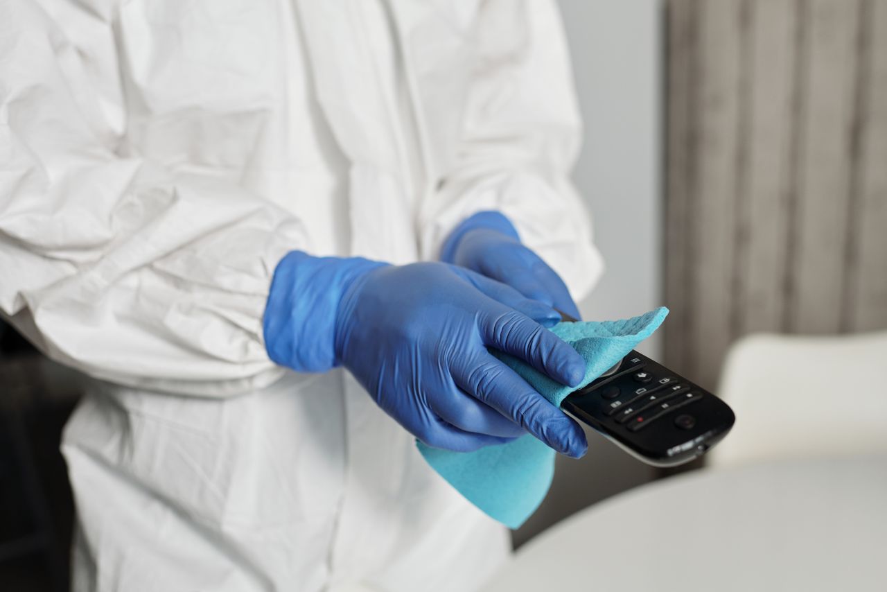 Close-up of a person disinfecting a remote control wearing protective gloves, ensuring cleanliness.
